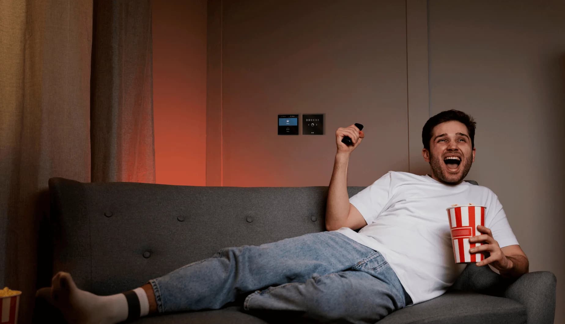 A man enjoying movie while having popcorns with MTronic Smart Dimmer and MTronic LCD Touch Panel installed and Movie scene activated